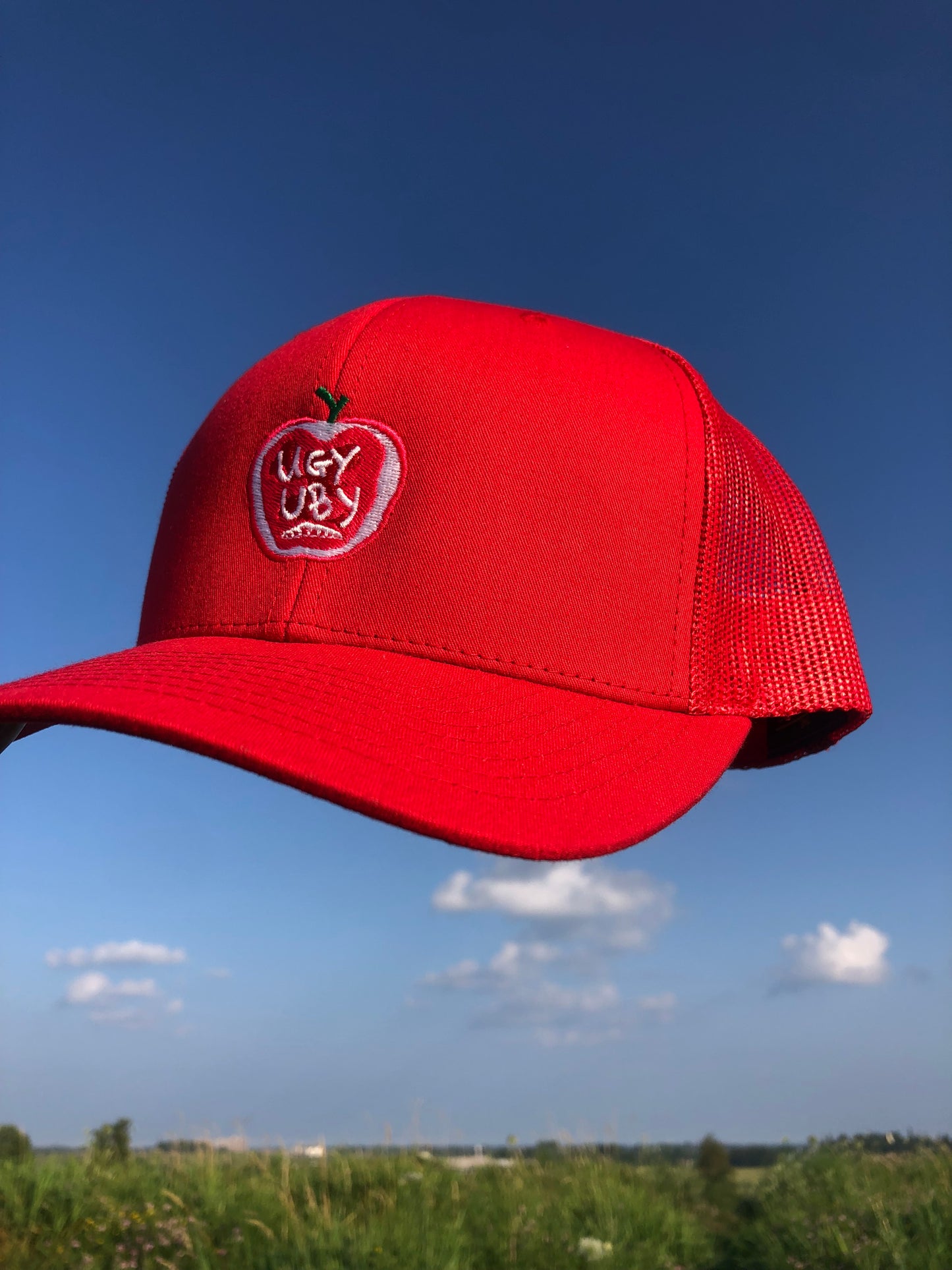red trucker hat with mesh backing floating in the blue sky over white puffy clouds